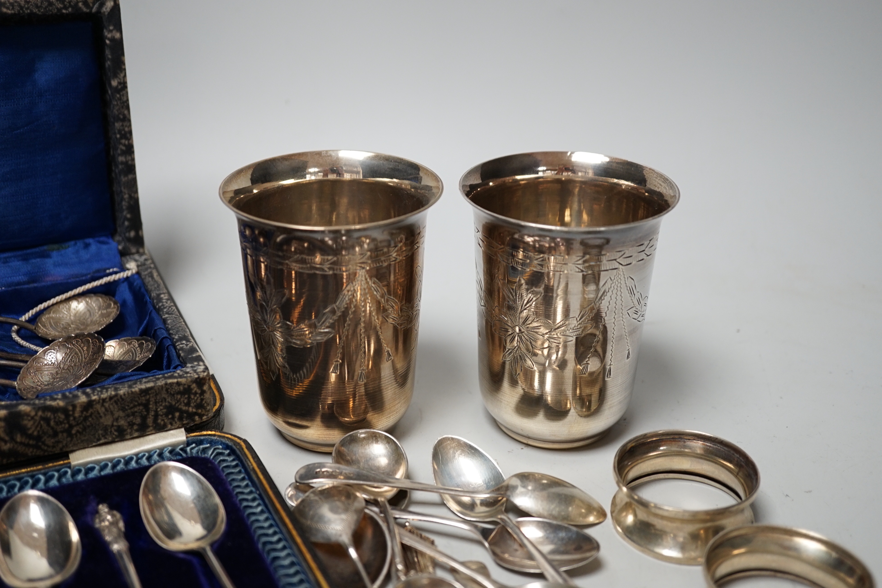 A pair of engraved white metal tumblers, stamped 'K980', four Russian 84 zolotnik spoon, a cased set of silver silver teaspoons with tongs, two silver napkin rings and other minor silver and white metal flatware.